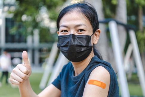 Vaccine Jab Thumbs Up lady in mask with orange bandaid after vaccine
